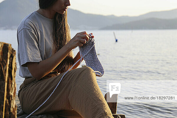 Young woman knitting in front of sea