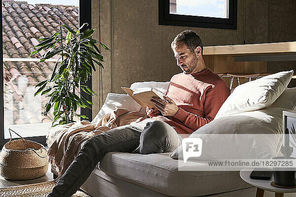 Man sitting on sofa reading book at home