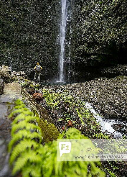 Hikers in front of a waterfall on a steep rock face  Levada do Caldeirão Verde  Parque Florestal das Queimadas  Madeira  Portugal  Europe