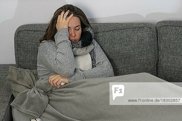 Kranke Frau mit Seidenpapier und ihrer mit einer Decke zugedeckten Katze auf ihrem Sofa