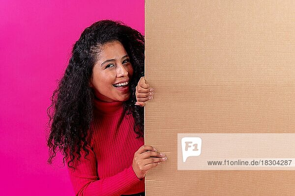 Gelockte Frau hält ein Schild lächelnd auf einem rosa Hintergrund  Studioaufnahme