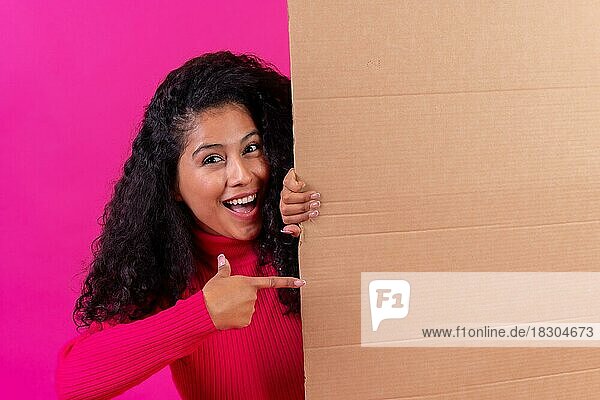 Lockenköpfige Frau  die auf ein Schild zeigt  lächelnd auf einem rosa Hintergrund  Studioaufnahme
