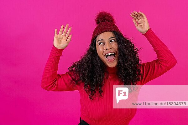 Porträt einer lockigen Frau mit Wollmütze vor einem rosa Hintergrund  die sich amüsiert  Studioaufnahme