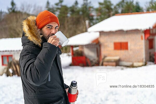 Mann trinkt Kaffee aus einer heißen Thermoskanne im Winter im Schnee neben einer Hütte  Artikutza  Gipuzkoa