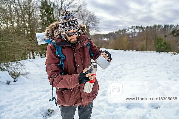 Mann frühstückt einen heißen Kaffee aus einer Thermoskanne im Winter im Schnee  bevor er zum Trekking aufbricht