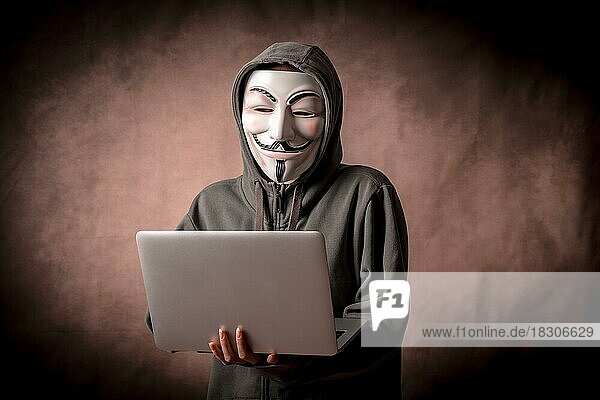 Mann mit anonymer Maske mit Sweatshirt und mit einem Laptop  Studioaufnahme
