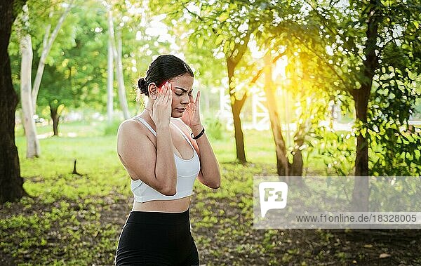 Athlete girl with migraine in a park. Young female runner rubbing her head with migraine in a park. Runner woman with headache and fatigue in the park  Runner woman with headache in a park