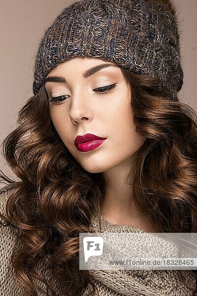 Schönes Mädchen mit sanftem Make-up  Locken in brauner Winterstrickmütze. Warmes Winterbild. Schönes Gesicht. Bild im Studio aufgenommen