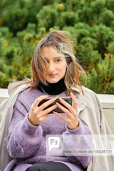 Junge Frau sitzt auf einer Bank und spielt ein Spiel oder sieht sich ein Video auf dem Smartphone an