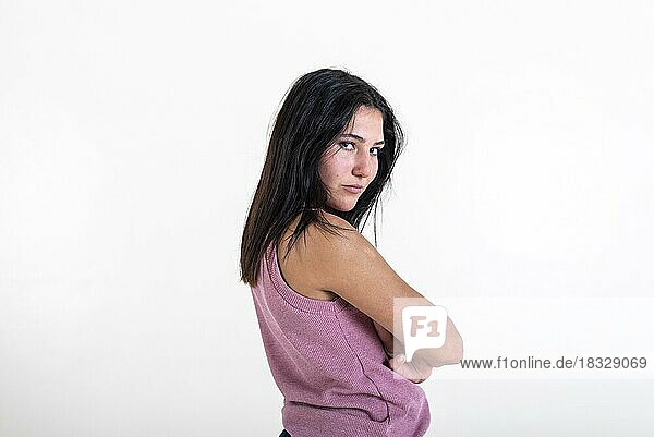 Beautiful young woman looking at camera with her arms folded  wearing a pink t-shirt. Studio shot. White background