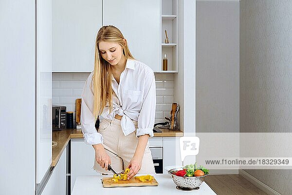 Junge Frau schneidet Paprika für einen Salat auf einem hölzernen Schneidebrett. Natürliche Zutaten  rohes veganes Gemüse