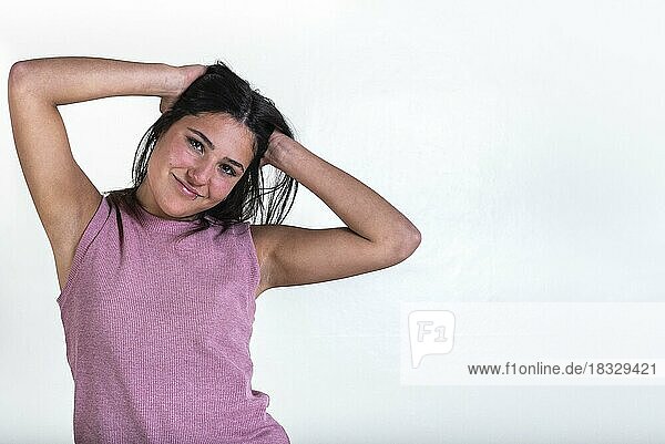 Beautiful young smiling woman wearing a pink t-shirt and with hands on her hair while she is looking at the camera over white background. Copy Space. Studio shot