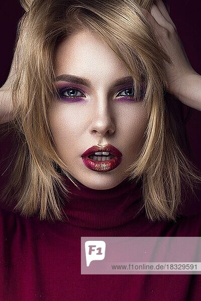 Schöne blonde Frau in einem roten Pullover mit hellem Make-up und dunklen Lippen. Schönes Gesicht. Bild im Studio aufgenommen