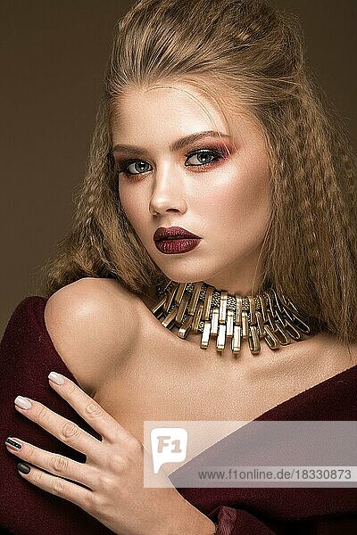 Schöne blonde Modell mit Locken  hellen Make-up  Goldschmuck und roten Lippen. Die Schönheit des Gesichts. Porträtaufnahme im Studio auf einem braunen Hintergrund