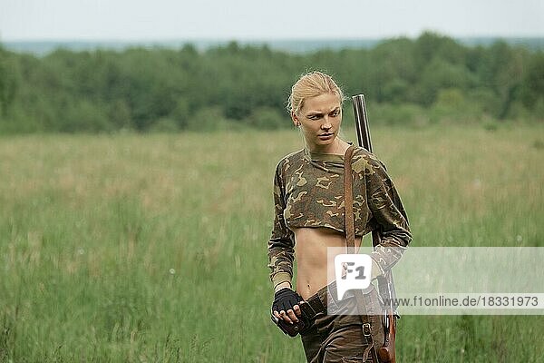 Attractive hunter girl with hunting double-barreled rifle walking along the field