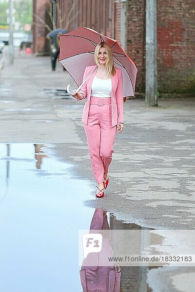 Frau in rosa Anzug mit Regenschirm zu Fuß auf der Straße nach dem regen