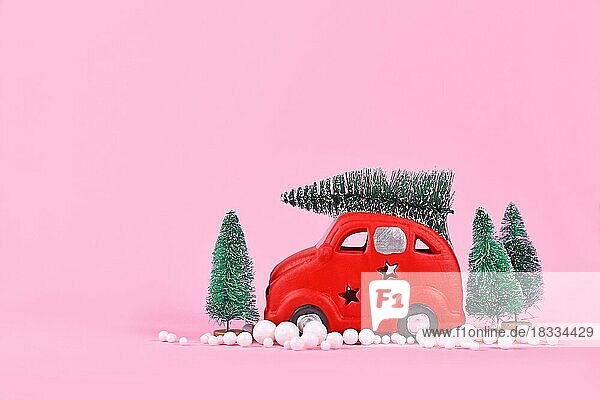 Miniatur-rotes Auto transportiert Weihnachtsbaum auf rosa Hintergrund