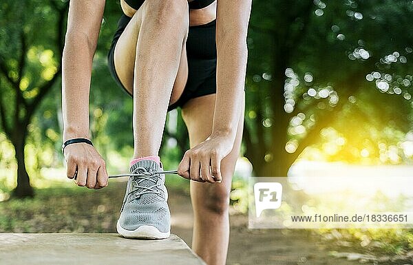 Nahaufnahme einer sportlichen Frau  die ihre Schuhe bindet. Sportliches Mädchen bindet ihre Schnürsenkel in einem Park. Läuferin bindet ihre Laufschuhe in einem Park mit Kopierraum
