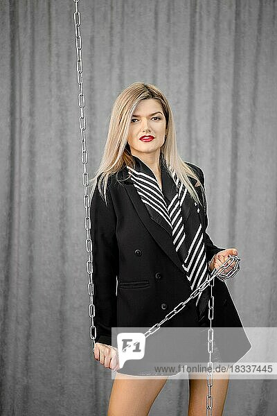 Starke Frau in schwarzer Jacke und Ledershorts hält Metallkette in Händen