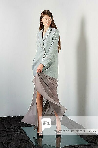 Attraktive Mode-Modell winkte ihr langes Spitzenkleid und Jacke posiert für Lookbook in der Nähe von grauen Wand