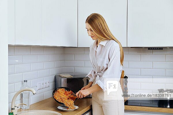 Junge Frau legt Spaghetti aus einer Bratpfanne auf einen Teller