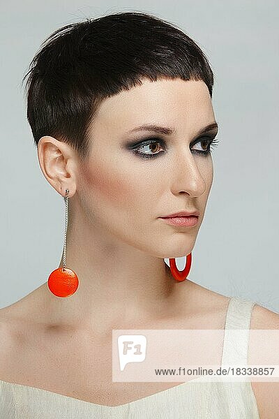 Hübsche junge Frau mit kurzen schwarzen Haaren und roten Ohrringen. Kurzer Haarschnitt und Stil  natürliches Make-up