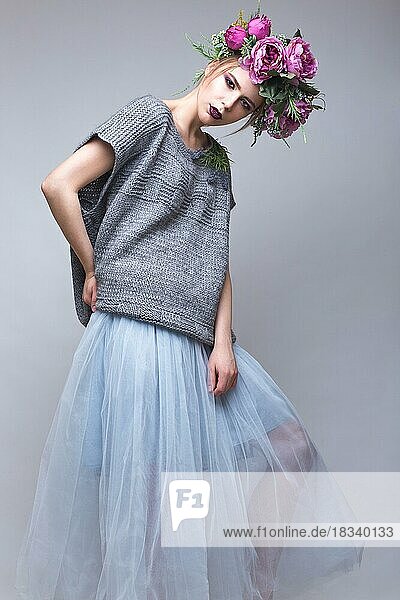 Schönes Mädchen mit Blumen auf dem Kopf in Mode Kleidung posiert gegen den Hintergrund im Studio. Schönheit Stil