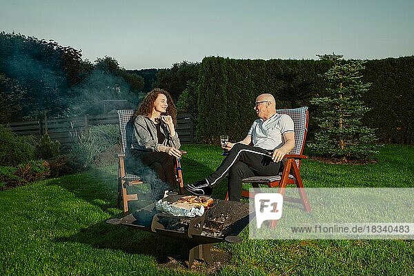 Happy couple barbecuing outdoors. Man turning sausages on grill