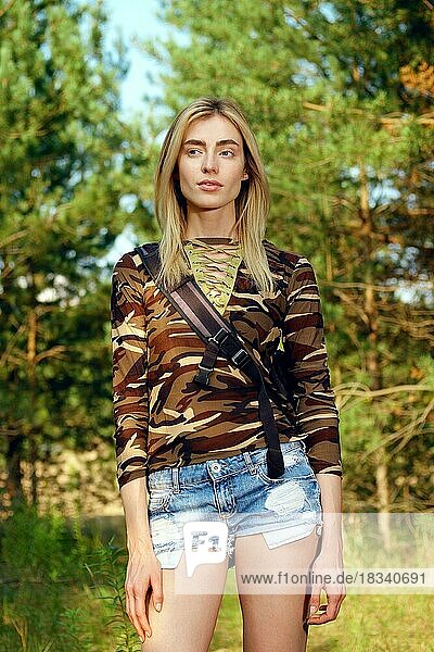 Attraktives Mädchen in Camouflage-Shirt  Jeans-Shorts mit Rucksack auf Wanderweg im Wald