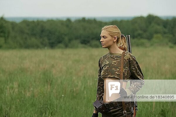 Attractive hunter girl with hunting double-barreled rifle walking across the field