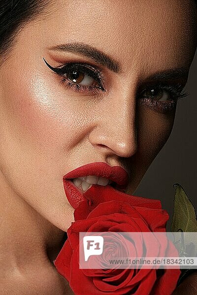 Schöne brünette Frau mit klassischem Make-up  roten Lippen und Blumen in der Hand. Die Schönheit des Gesichts. Porträtaufnahme im Studio