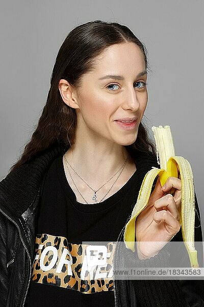 Hübsches Mädchen in Lederjacke beißt frische Banane. sauberes natürliches Make-up  lange Haare  blaue Augen