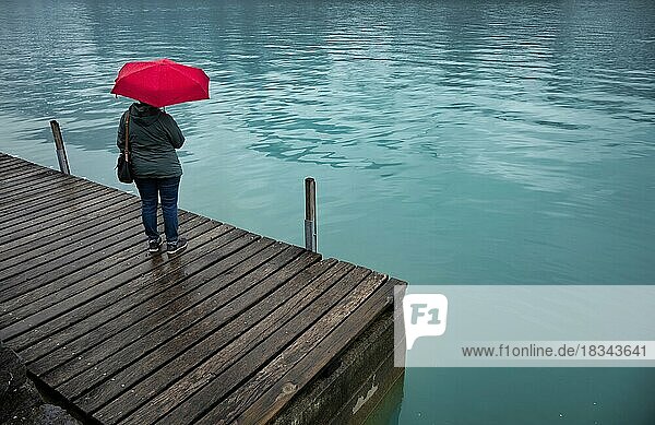 Ältere Frau  Best-Ager  mit rotem Regenschirm  schlechtes Wetter  Seepromenade am Brienzersee  Brienz  Kanton Bern  Berner Oberland  Schweiz  Europa