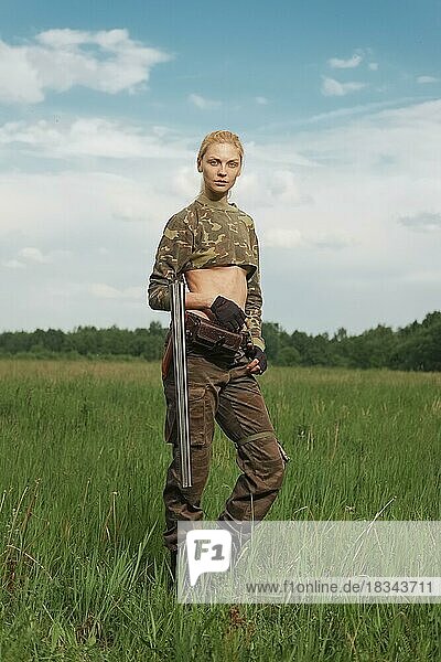 Attraktives Jägermädchen mit doppelläufigem Jagdgewehr geht über das Feld