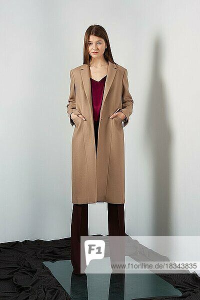 Attraktive Mode-Modell in Hosen  Bluse auf Trägern und Licht Mantel posiert für Lookbook in der Nähe von grauen Wand