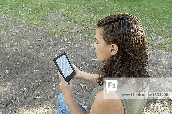 Junge Frau liest ein E-Book im Park. Raum kopieren