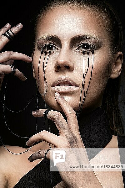 Beautiful girl with creative make-up in Gothic style and the threads of eyes. Art beauty face. Picture taken in the studio on a black background