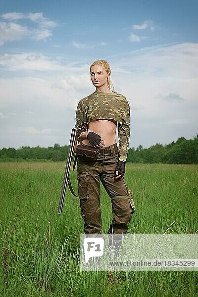 Attractive hunter girl with hunting double-barreled rifle walks across the field