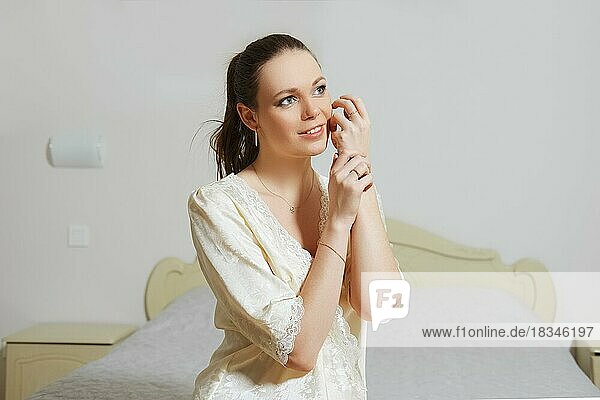 Pretty young lady in bedroom in silk peignoir sits on the couch near the bed