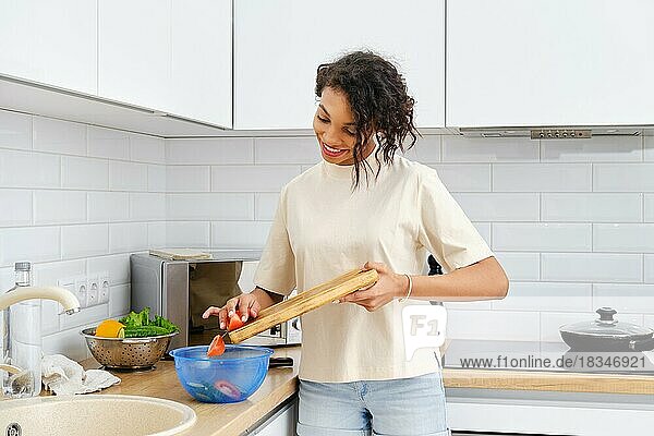 Junge afroamerikanische Frau wirft gehackte Tomaten in die Schüssel in der Küche