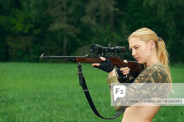 Pretty hunter girl aiming with hunting rifle in the outer wood. Carbine with optical-sight
