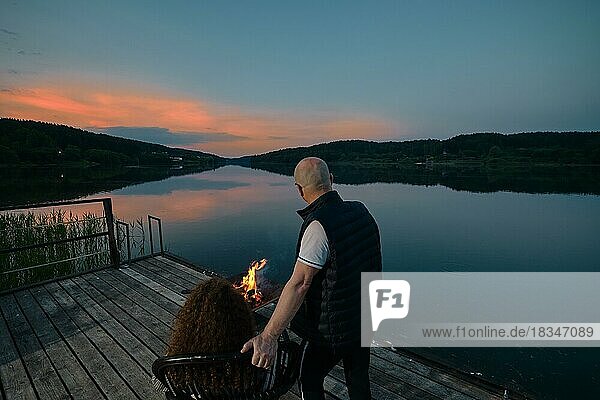 Niedliches Paar beobachtet den Sonnenuntergang am Feuer sitzend auf dem Pier  Rückansicht