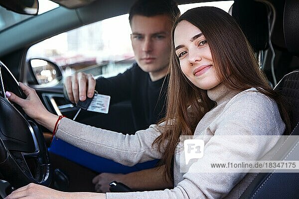 Glückliches Mädchen in einem neuen Auto erhält von einem jungen Mann einen Führerschein und Schlüssel