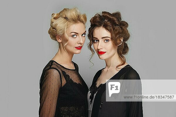 Zwei hübsche Mädchen mit lockigem Haar flirten. Blonde und brünette Mädchen mit natürlichem Make-up und roten Lippen