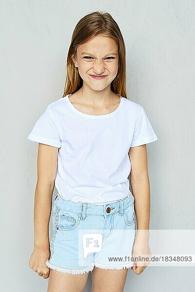 Young angry and mischievous girl in white t-shirt and jeans shorts posing in studio