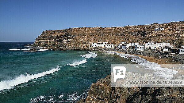 Puertito de los Molinos  ganzer Strand  Wellen  Brandung  mehrere kleine weiße Häuser  blauer wolkenloser Himmel  Westküste  Fuerteventura  Kanarische Inseln  Spanien  Europa
