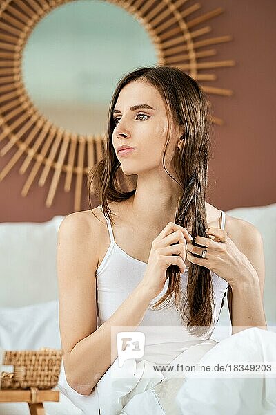 Mädchen sitzt auf dem Bett und flechtet Haare zu einem Zopf