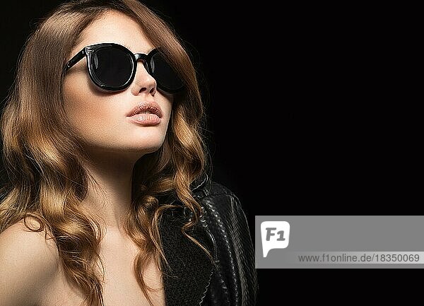 Beautiful girl in dark sunglasses  with curls and evening makeup. Beauty face. Picture taken in the studio on a black background