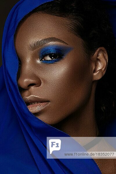 Schöne schwarze Frau mit blauem Stoff und klassischem Kunst-Make-up. Schönes Gesicht. Foto im Studio aufgenommen