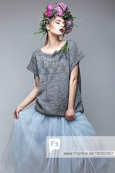 Schönes Mädchen mit Blumen auf dem Kopf in Mode Kleidung posiert gegen den Hintergrund im Studio. Schönheit Stil